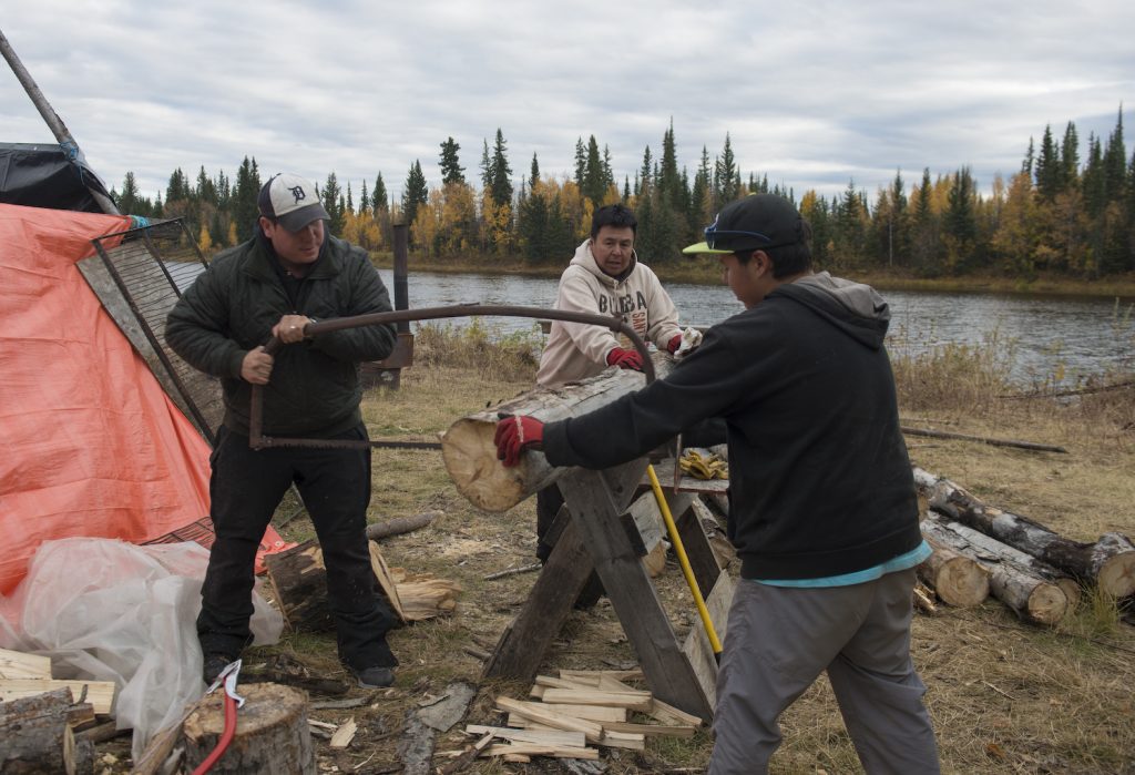 Pat Kane, Lloyd Chicot, Tarek Chico cutting firewood at a hunting camp on Tathlina Lake in the Northwest Territories.