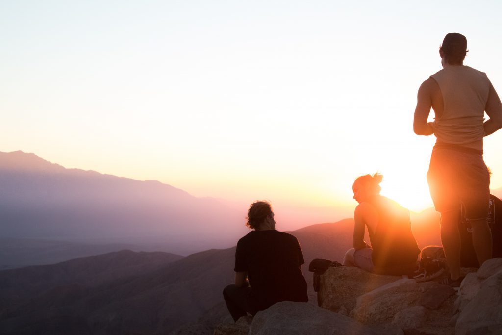 three people sitting on rocks on a hill while the sun sets.