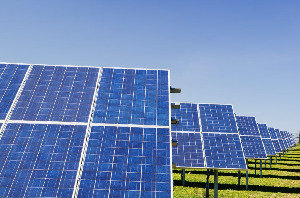 This photo shows a role of solar panels. The grass is green and the sky is bright blue.