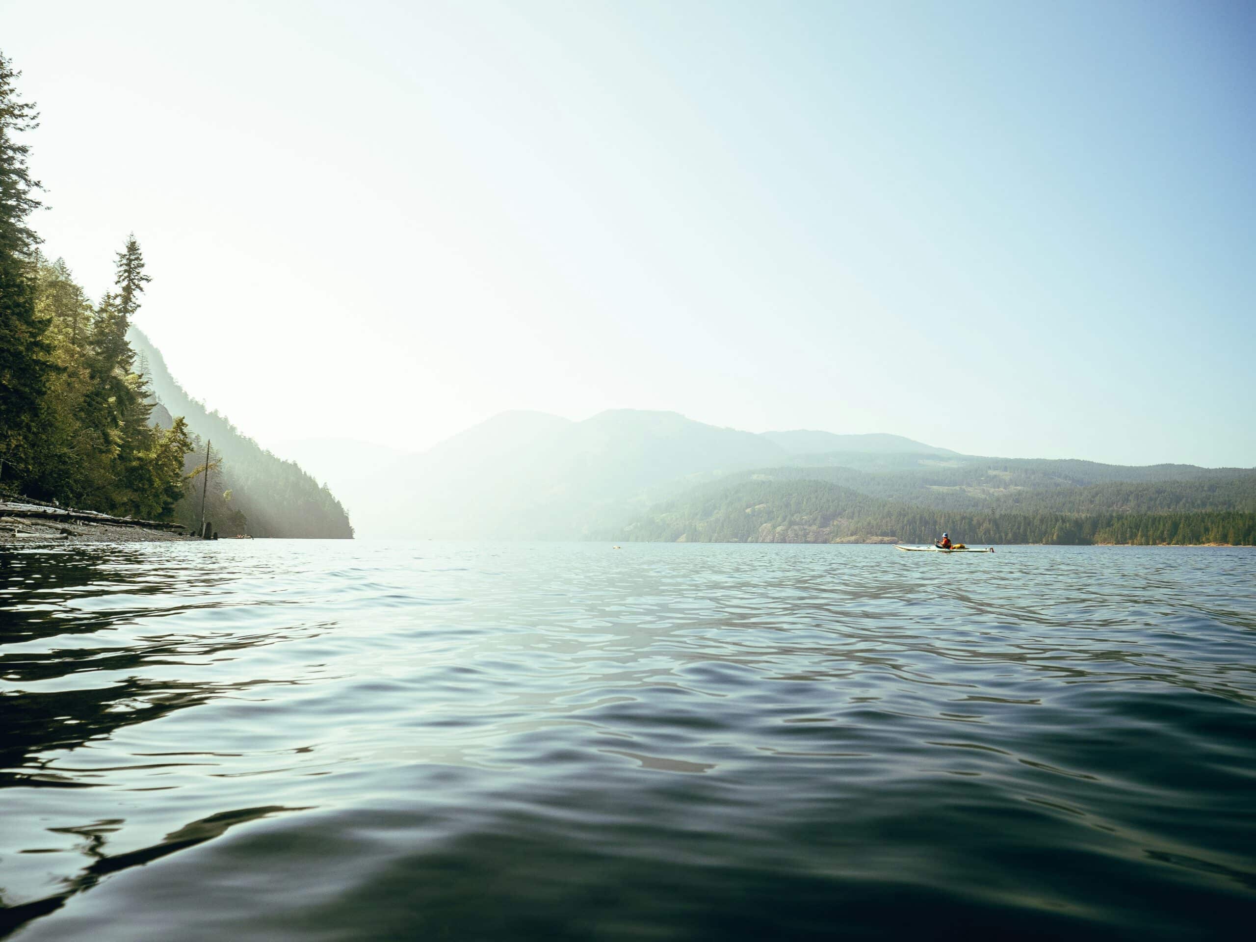 A water body in the foreground with mountains in the distance. Photo by Devon Hawkins