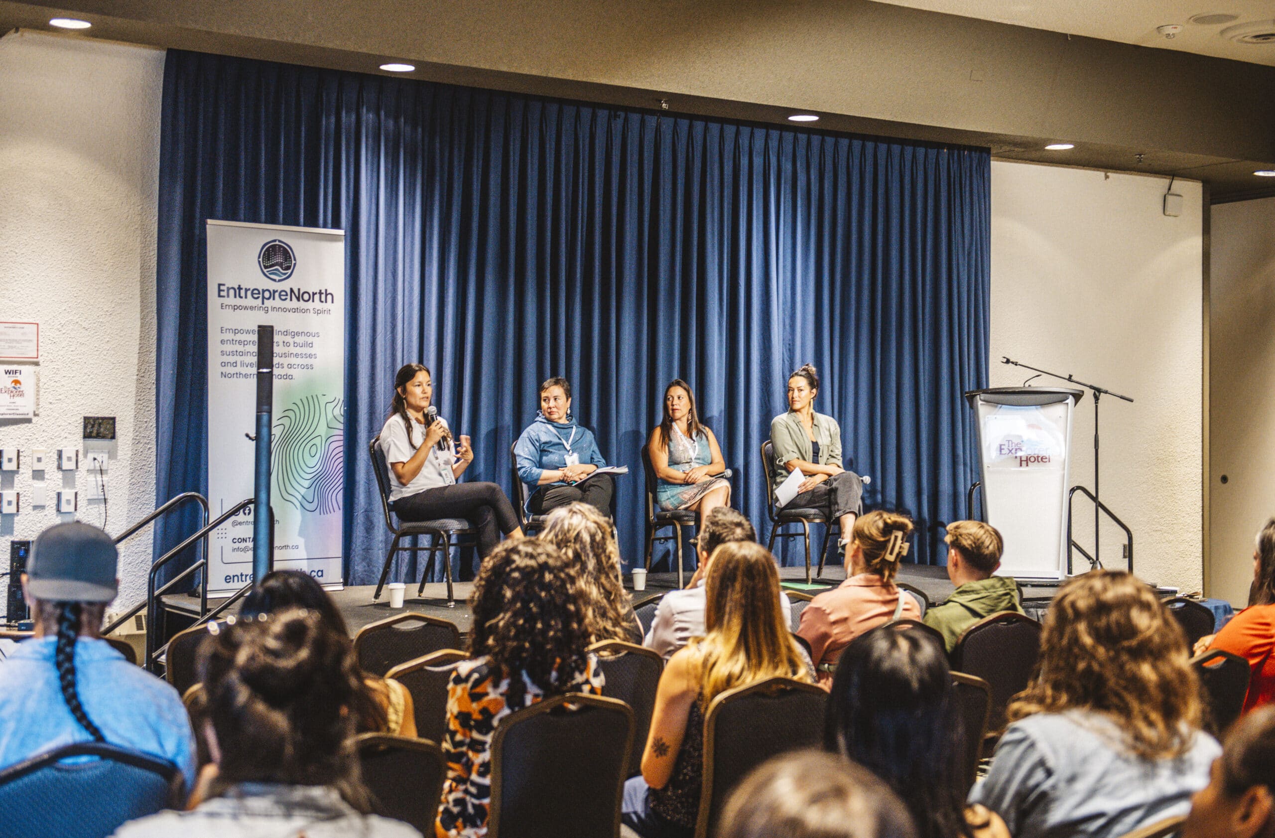 4 panel members are seated on a stage in front of and audience