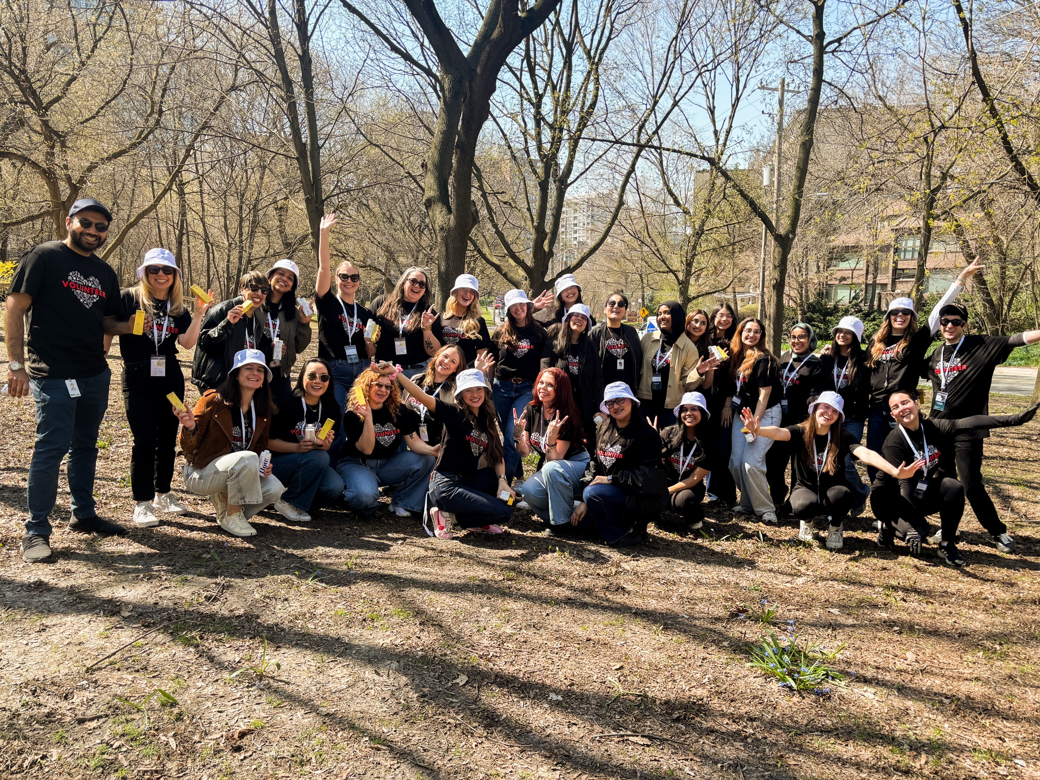 A group of volunteers in matching black shirts smiling at the camera. The picture is taken in a large park with trees behind them.